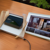 A table with two picture frames with different sizes and one of them is a picture of a house.