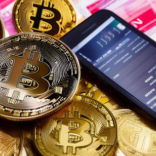 Gold and black bitcoin coins are piled on top of each other and next to a smart phone.