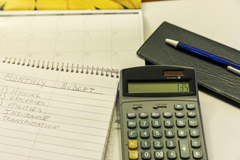 A spiral notebook with a pen and calculator on top of it.