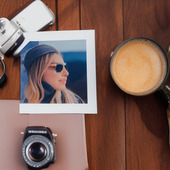 A photo of a woman with sunglasses sits on a wooden table, next to a camera.