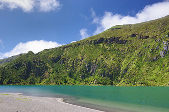 A view of a rocky coastline, overlooking a body of water. The green grass on the mountain side is lush and colorful.
