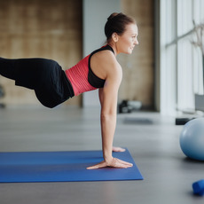 A woman in a pink sports bra is doing a push-up in a gym.