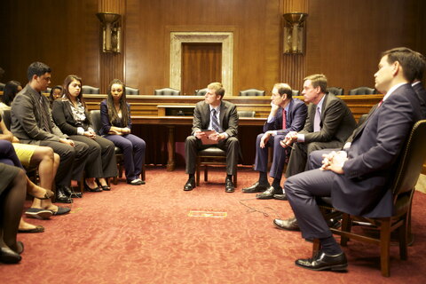 A group of people in a room, some seated on chairs while others are standing around.